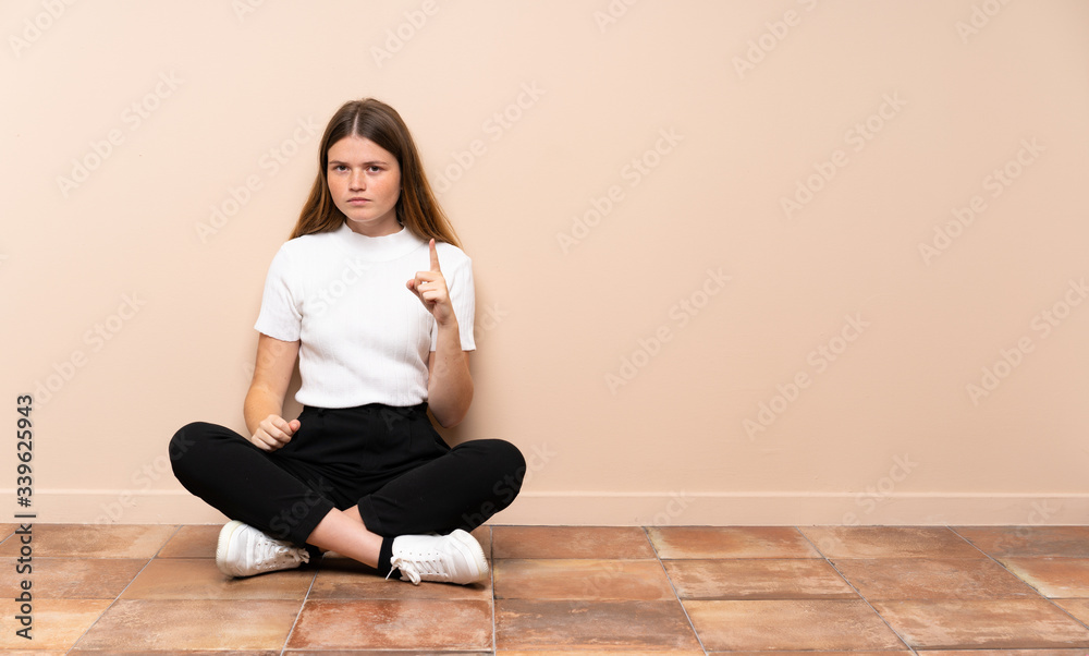 Ukrainian teenager girl sitting on the floor frustrated and pointing to the front Ukrainian teenager girl sitting on the floor frustrated and pointing to the front
