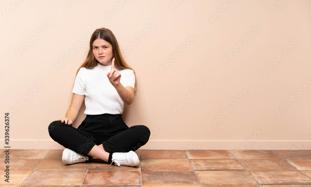 Ukrainian teenager girl sitting on the floor showing and lifting a finger Ukrainian teenager girl sitting on the floor showing and lifting a finger