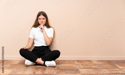 Ukrainian teenager girl sitting on the floor showing a sign of silence gesture putting finger in mouth