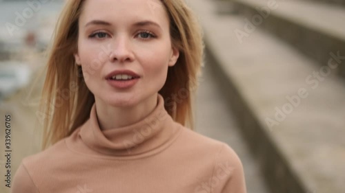 Close up shot of pretty blond girl in throat sweater looking in camera and smiling walking outdoor 