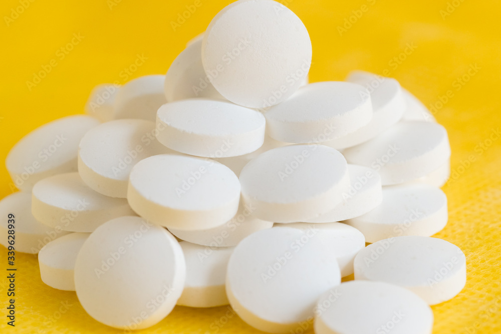 A mountain of scattered white round tablets on a yellow background A mountain of scattered white round tablets on a yellow background