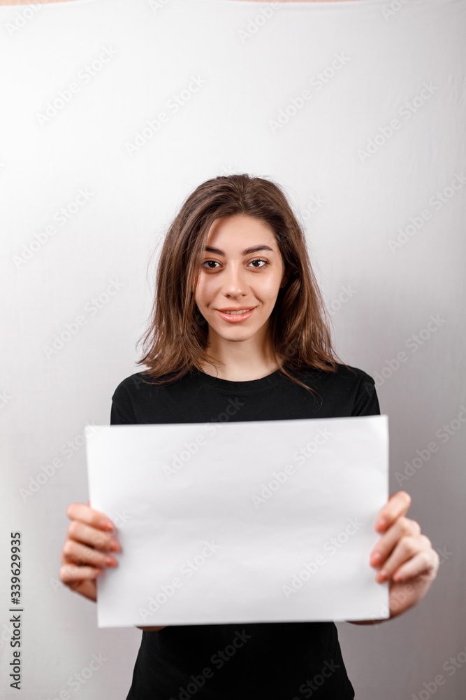 young brunette woman in a black t-shirt smiling shows a white sheet on a white background. copyspase young brunette woman in a black t-shirt smiling shows a white sheet on a white background. copyspase
