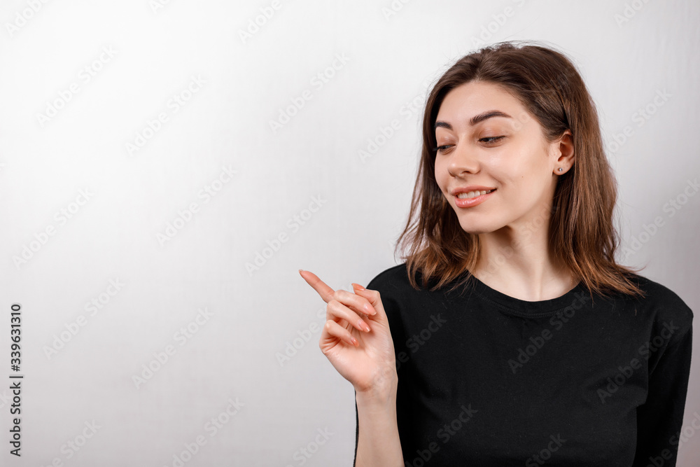 smiling young brunette woman shows finger to the side on a white background copyspase smiling young brunette woman shows finger to the side on a white background copyspase