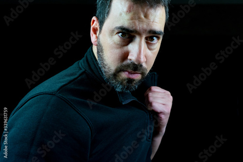 Portrait of bearded man dressed in black sweatshirt on a black background in defiant attitude photo