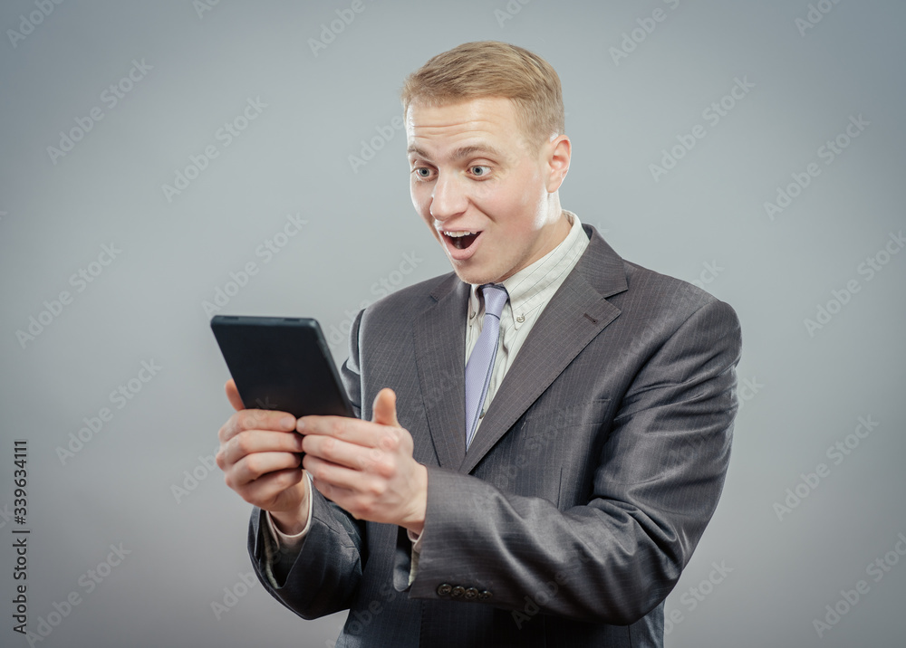 Successful businessman standing using a tablet to access the internet as he leans Successful businessman standing using a tablet to access the internet as he leans