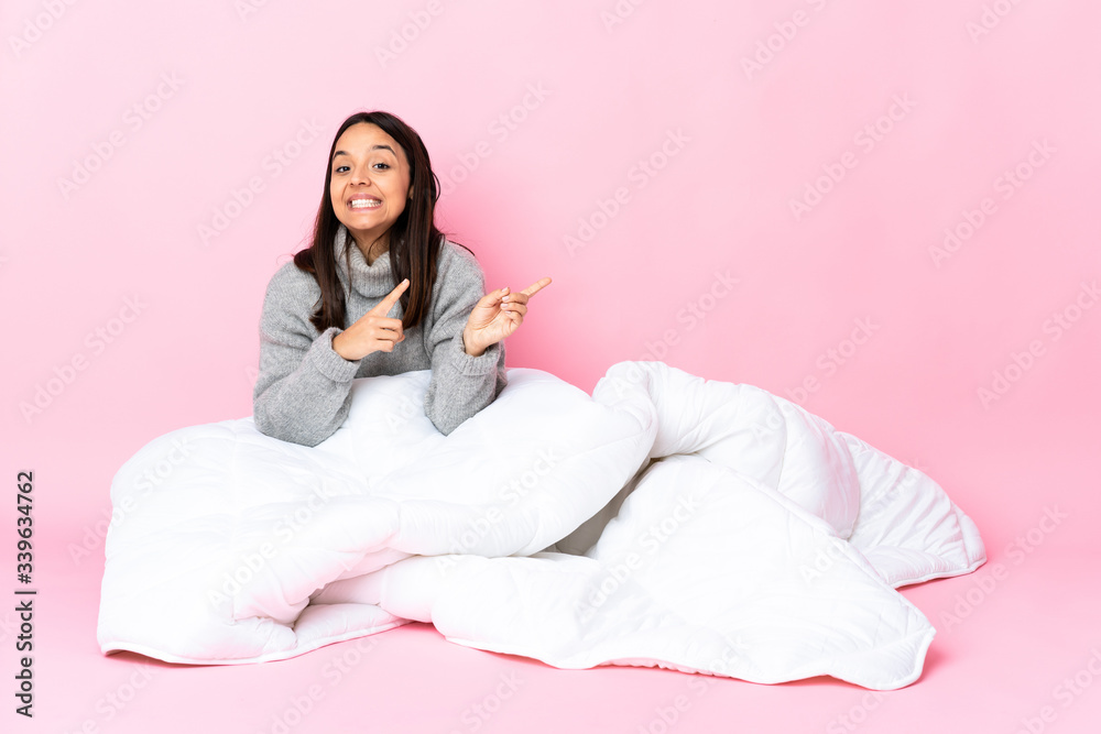 Young mixed race woman wearing pijama sitting on the floor frightened and pointing to the side Young mixed race woman wearing pijama sitting on the floor frightened and pointing to the side