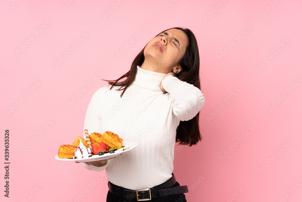 Young brunette woman holding waffles over isolated pink background with neckache