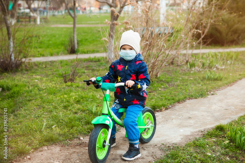 quarantine. A boy in a medical mask on a runbike walks along the street near the house during quarantine of the coronavirus. The ability to go for a walk with safety measures photo