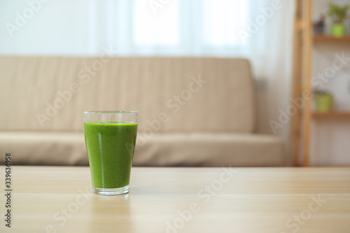 Glass of green smoothie or cocktail on wooden table in living room