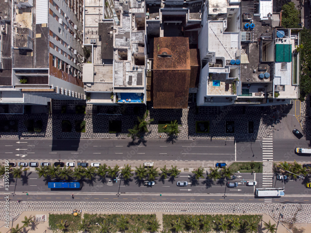 Avenue in Ipanema, Rio de Janeiro, seen from top down with palm trees between the roads and along the beach with high rise buildings casting a dark shadow on the sidewalk Avenue in Ipanema, Rio de Janeiro, seen from top down with palm trees between the roads and along the beach with high rise buildings casting a dark shadow on the sidewalk