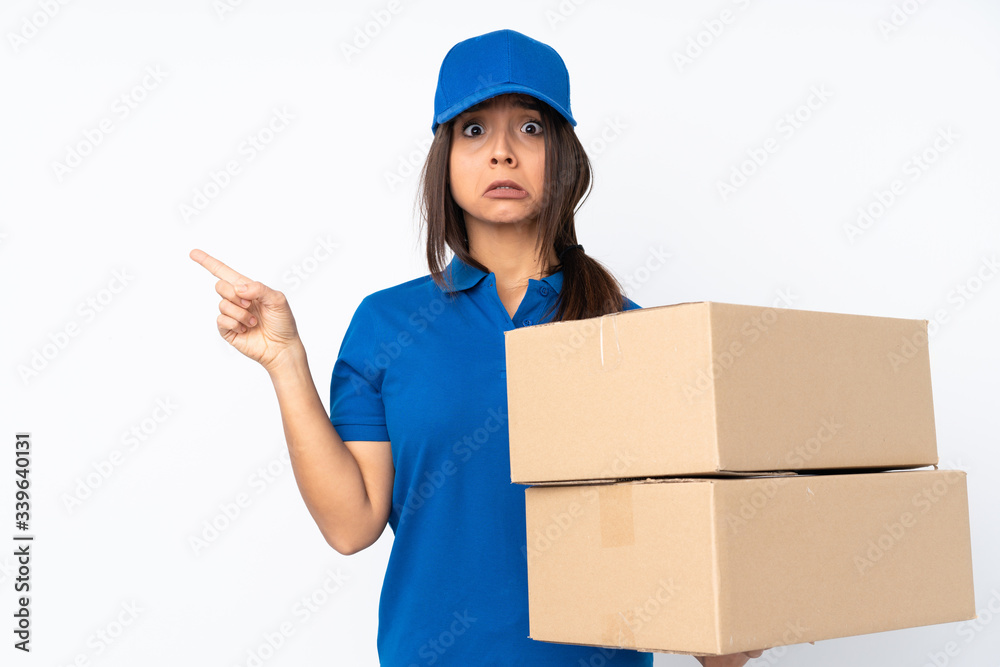 Young delivery brunette girl over isolated white background frightened and pointing to the side Young delivery brunette girl over isolated white background frightened and pointing to the side