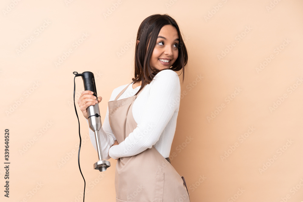 Young brunette girl using hand blender over isolated background with arms crossed and happy Young brunette girl using hand blender over isolated background with arms crossed and happy
