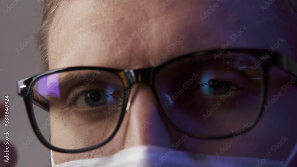 Macro: A man wearing glasses and a mask scornfully looks into the camera and takes off his glasses Macro: A man wearing glasses and a mask scornfully looks into the camera and takes off his glasses