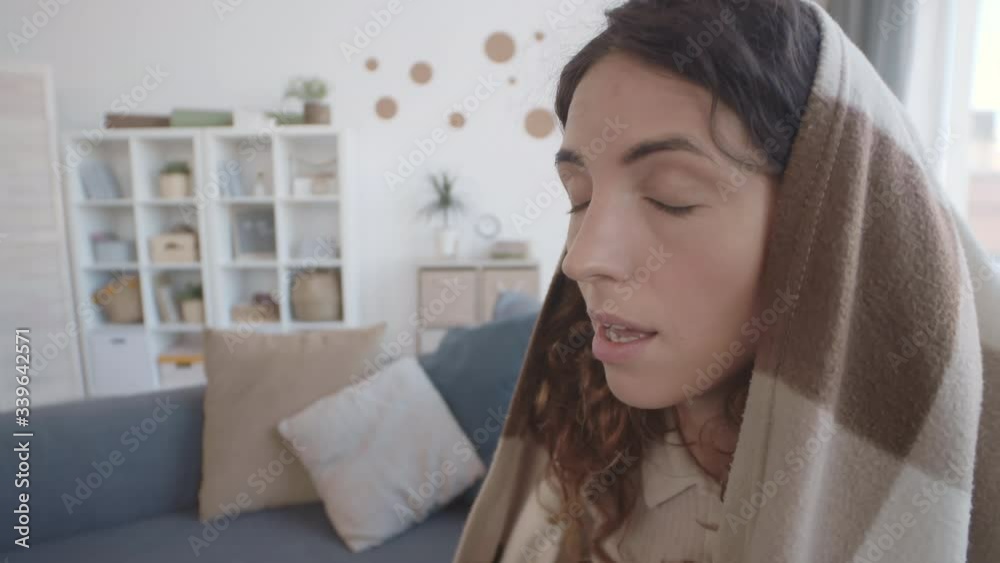 Close up of Caucasian young woman covered with blanket sneezing and wiping her nose with napkin Close up of Caucasian young woman covered with blanket sneezing and wiping her nose with napkin