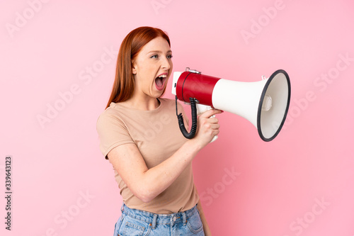 Young redhead woman over isolated pink background shouting through a megaphone