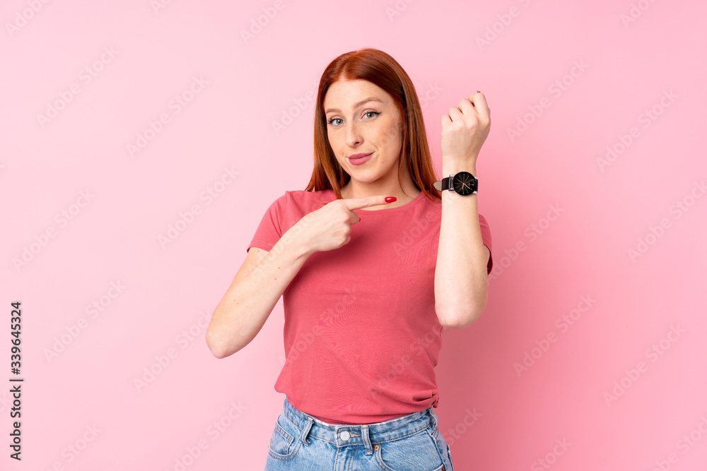 Young redhead woman over isolated pink background showing the hand watch Young redhead woman over isolated pink background showing the hand watch