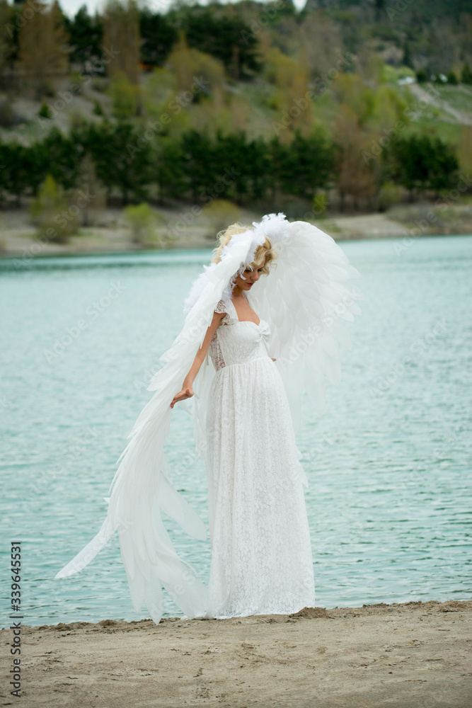 pregnant beautiful girl angel blonde in a white dress with wings stands by the lake pregnant beautiful girl angel blonde in a white dress with wings stands by the lake