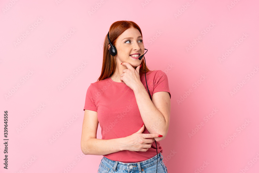 Young redhead woman over isolated pink background working with headset looking side Young redhead woman over isolated pink background working with headset looking side
