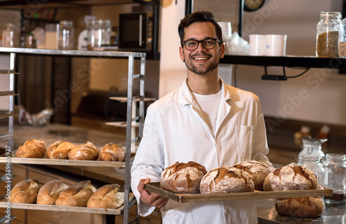 Fotografie, Obraz Portrait of young male baker holding bread in his hands at bakery