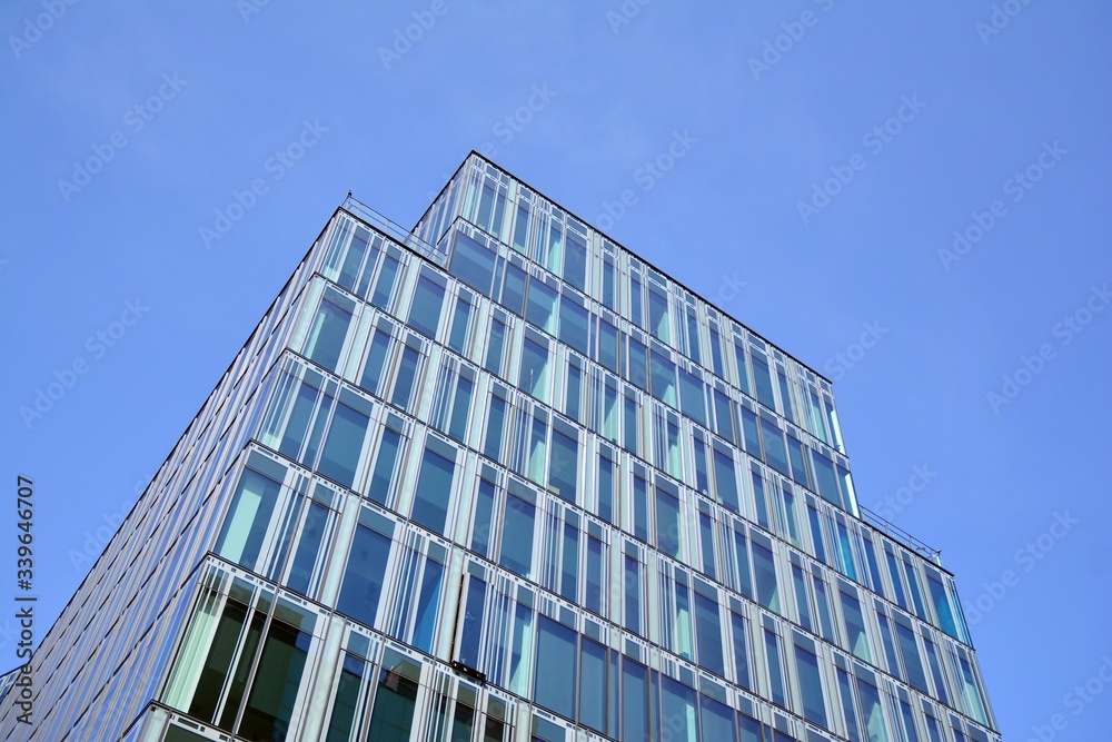 Blue curtain wall made of toned glass and steel constructions under blue sky. A fragment of a building. Blue curtain wall made of toned glass and steel constructions under blue sky. A fragment of a building.