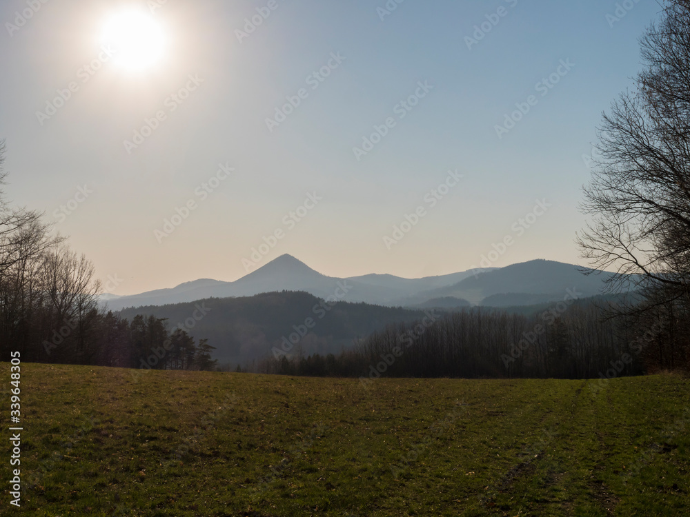 early spring landscape at Lusatian mountains, with view point hill klic, grass meadow, bare trees, deciduous and spruce tree forest, clear blue sky background, golden hour light, horizontal, copy