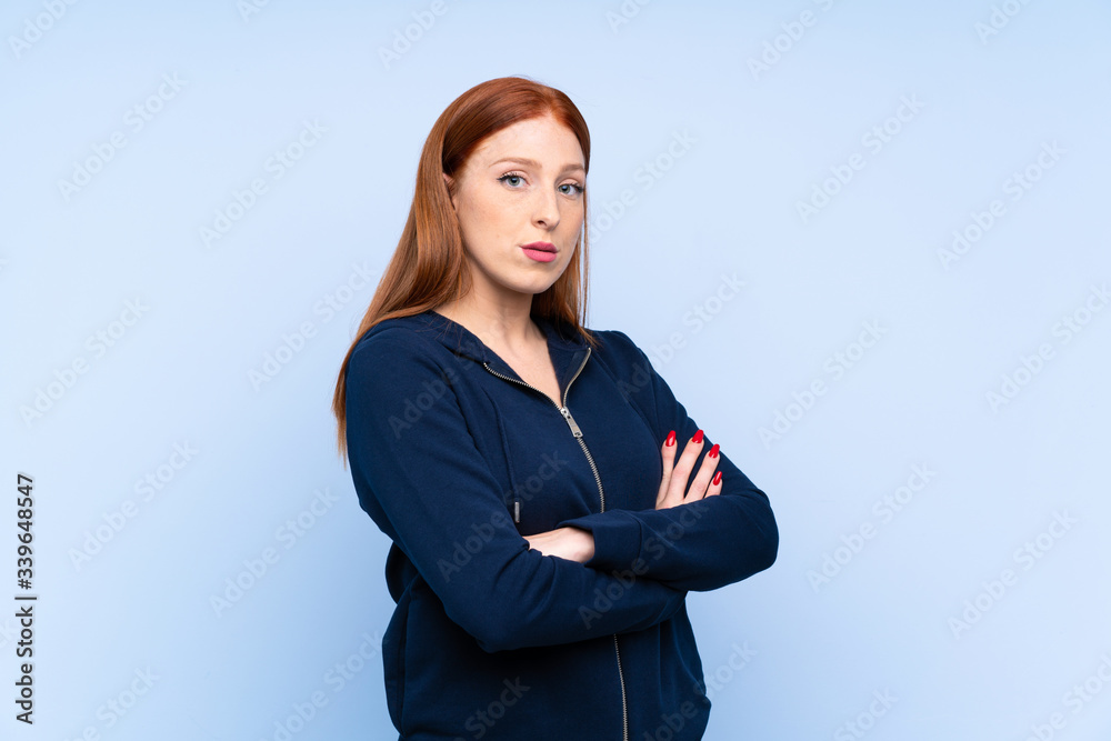 Young redhead sport woman over isolated blue background keeping the arms crossed Young redhead sport woman over isolated blue background keeping the arms crossed