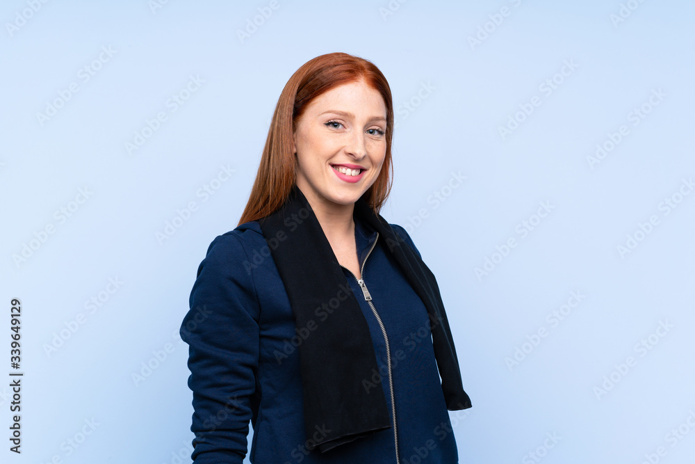 Young redhead sport woman over isolated blue background with sport towel Young redhead sport woman over isolated blue background with sport towel