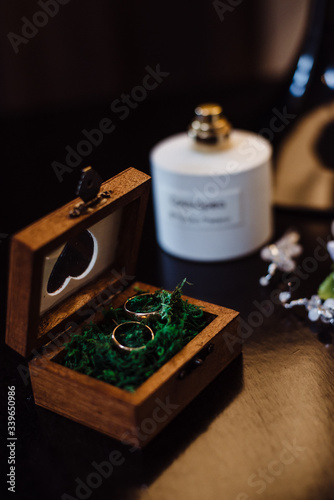Two gold wedding rings in a beautiful wooden casket with green moss. Wedding accessories. Bride morning. Film noise