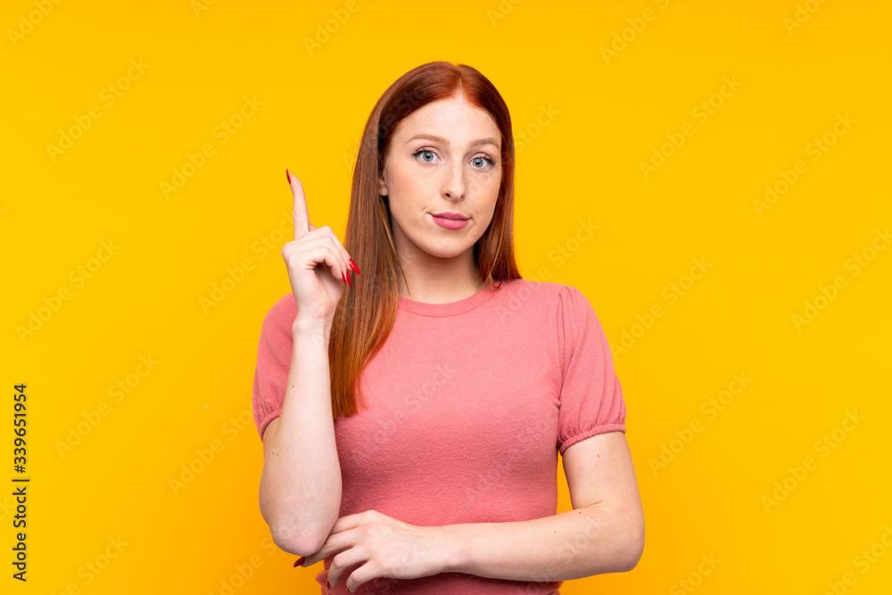 Young redhead woman over isolated yellow background pointing with the index finger a great idea Young redhead woman over isolated yellow background pointing with the index finger a great idea