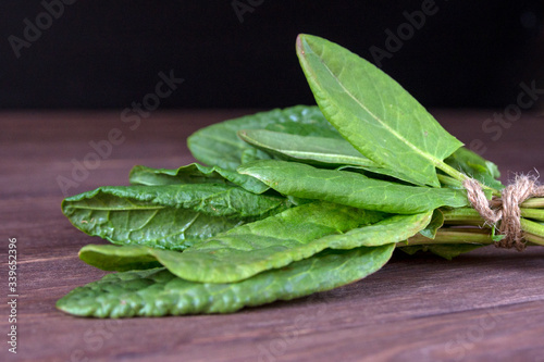 Young green leaves of sorrel tied in a pile on a wooden background. Useful vegetable culture and medicinal plant Rumex acetosa, rich in vitamins and minerals. photo