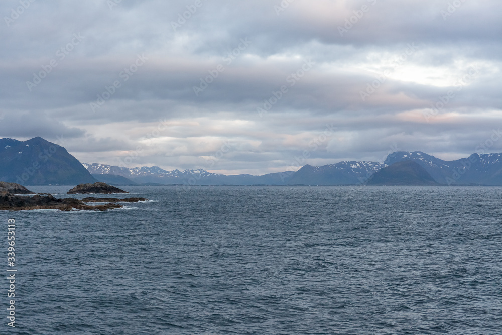 Norwegian fjord and mountains surrounded by clouds, midnight sun, polar day, ideal fjord reflection in clear water. selective focus.