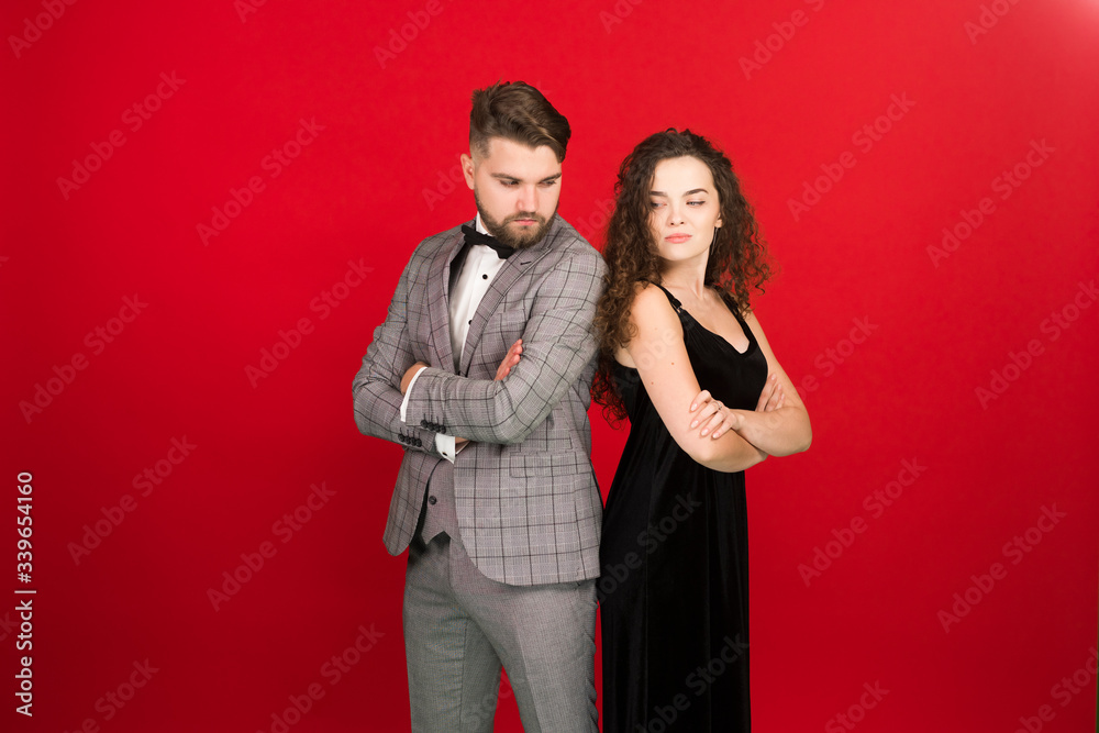 Upset couple with folded arms standing back to back isolated on red background Upset couple with folded arms standing back to back isolated on red background