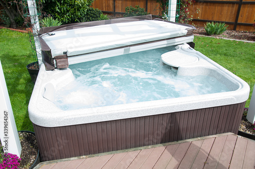 Hot tub in back yard with water bubbling and the lid half off, ready to be enjoyed in the outdoors.
