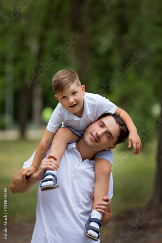 Father and his little son in white t-shirts playing outdoors. Little boy sitting on the shoulders of his father.