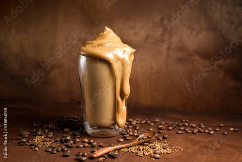 cold dalgona coffee in clear glasses on a dark wooden background. froth of sugar and instant coffee whipped with a mixer on top of cold milk. close up. copyspace