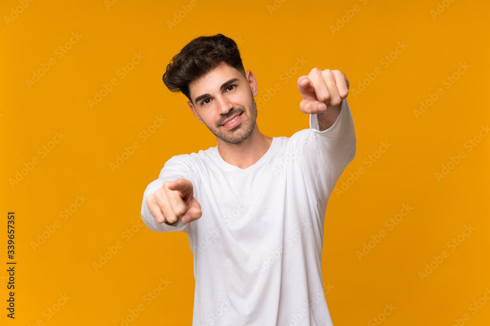 Young man over isolated orange background points finger at you while smiling Young man over isolated orange background points finger at you while smiling