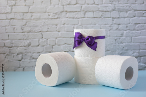 Four rolls of toilet paper on white brick wall background. Toilet roll with purple bow