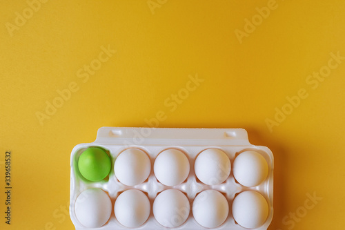 Packaging with a dozen eggs on a yellow background. One egg is painted green. Preparing for Easter.