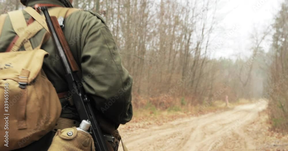 Historical Re-enactment. Re-enactors Dressed As American Soldiers Of USA Infantry Of World War II Marching Walking Along Forest Road In Autumn Day. Group of Soldiers Marching In Forest