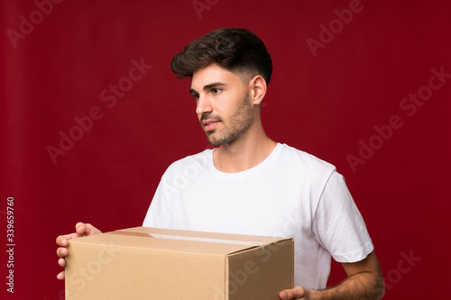 Young man over isolated background holding a box to move it to another site