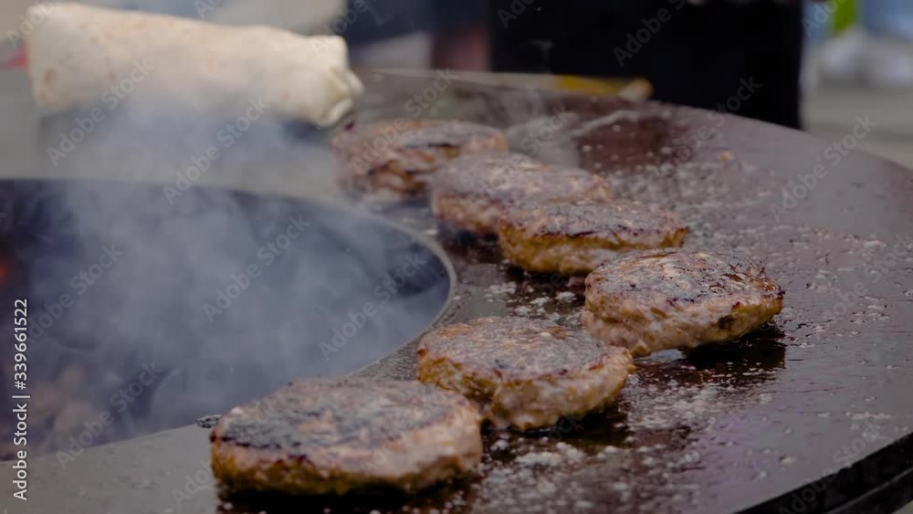 Super slow motion: process of grilling fresh meat cutlets for burgers on brazier with hot flame at summer local food market - close up view. Outdoor cooking, gastronomy, cookery, street food concept Super slow motion: process of grilling fresh meat cutlets for burgers on brazier with hot flame at summer local food market - close up view. Outdoor cooking, gastronomy, cookery, street food concept