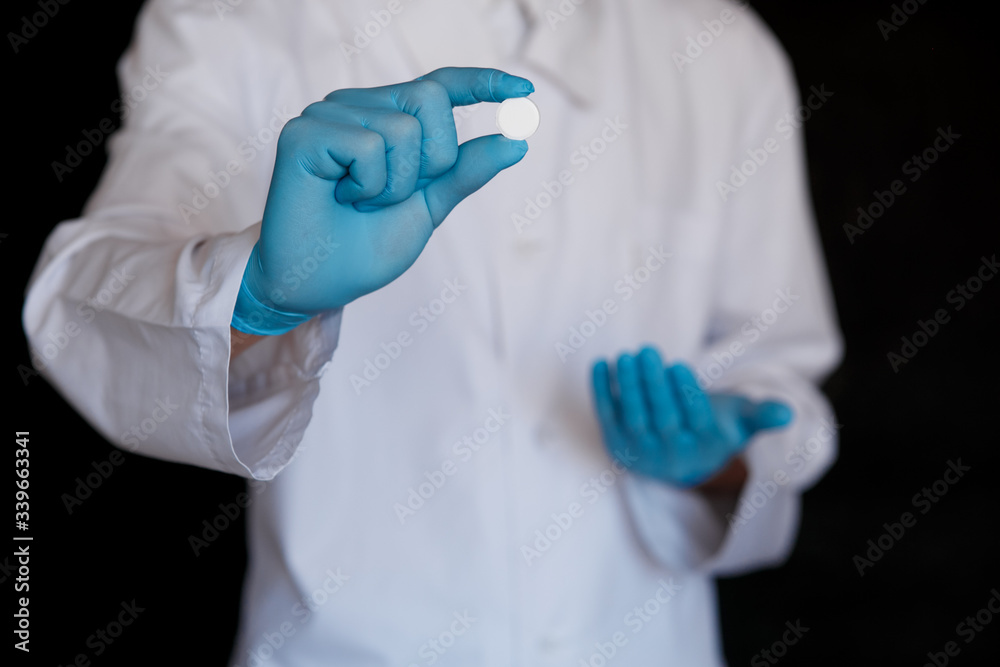Many small white pills in the hands of a doctor wearing medical blue disposable gloves. Hands take one pills Many small white pills in the hands of a doctor wearing medical blue disposable gloves. Hands take one pills