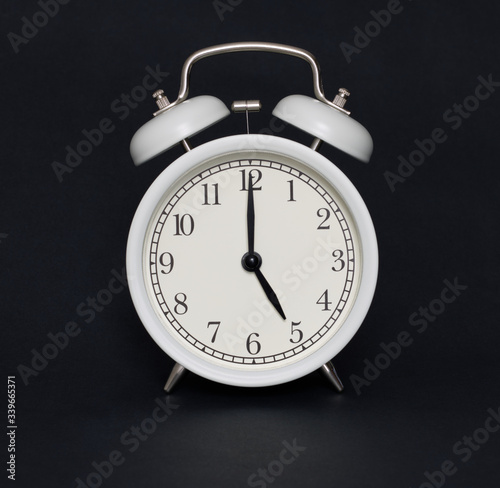 Old-style alarm clock, black and white, it's five o'clock.