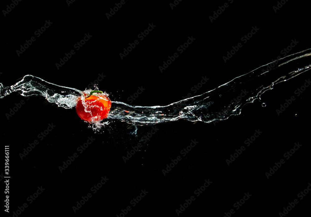 Fresh ripe red tomato with green leave flying in wave of water in the air isolated on black background. Concept of food levitation
