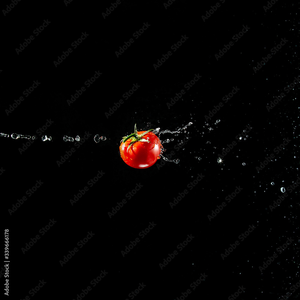 A fresh ripe red tomato with a green leaf flies in the air in water drops isolated on a black background. Concept of food levitation