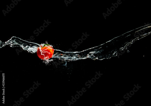 Obraz na płótnie Fresh ripe red tomato with green leave flying in wave of water in the air isolated on black background. Concept of food levitation w salonie