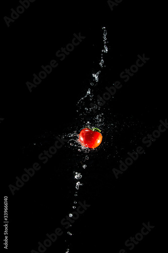 A fresh ripe red tomato with a green leaf flies in the air in water drops isolated on a black background. Concept of food levitation