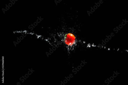 A fresh ripe red tomato with a green leaf flies in the air in water drops isolated on a black background. Concept of food levitation