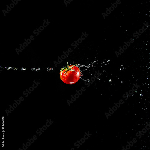 Obraz na płótnie A fresh ripe red tomato with a green leaf flies in the air in water drops isolated on a black background. Concept of food levitation w salonie