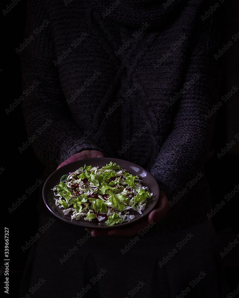 Green salad on a plate in the hands on a dark background, minimalism.
